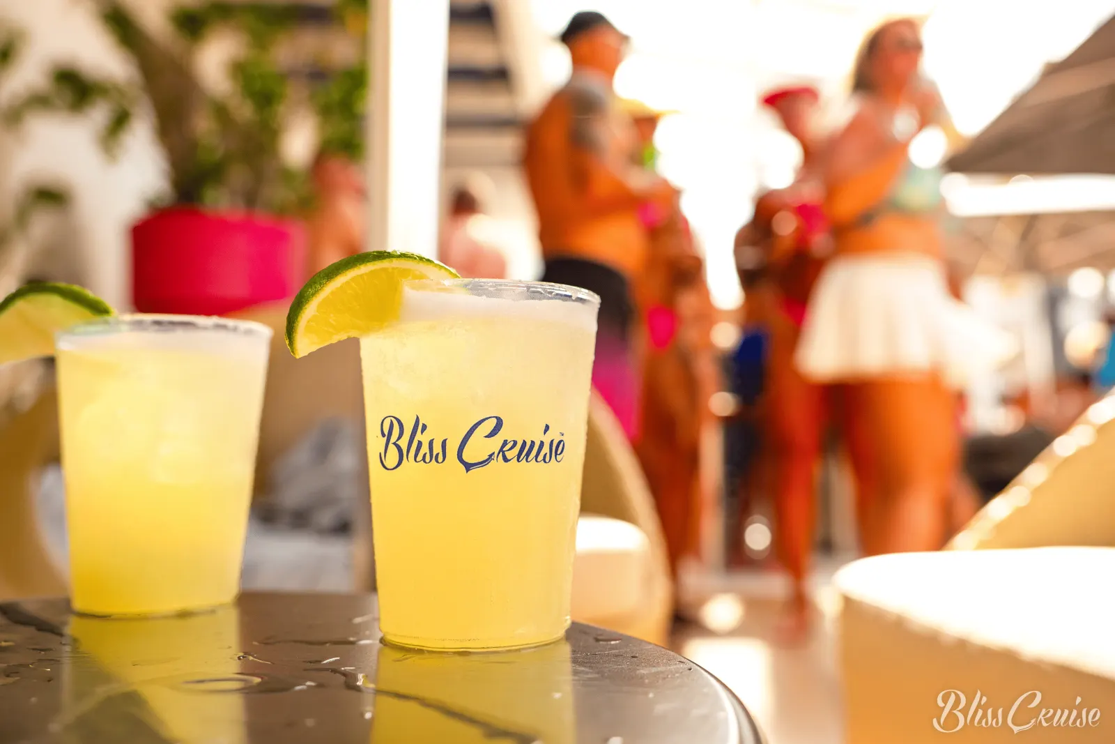 Two margaritas with lime in Bliss Cruise cups on a table by the pool